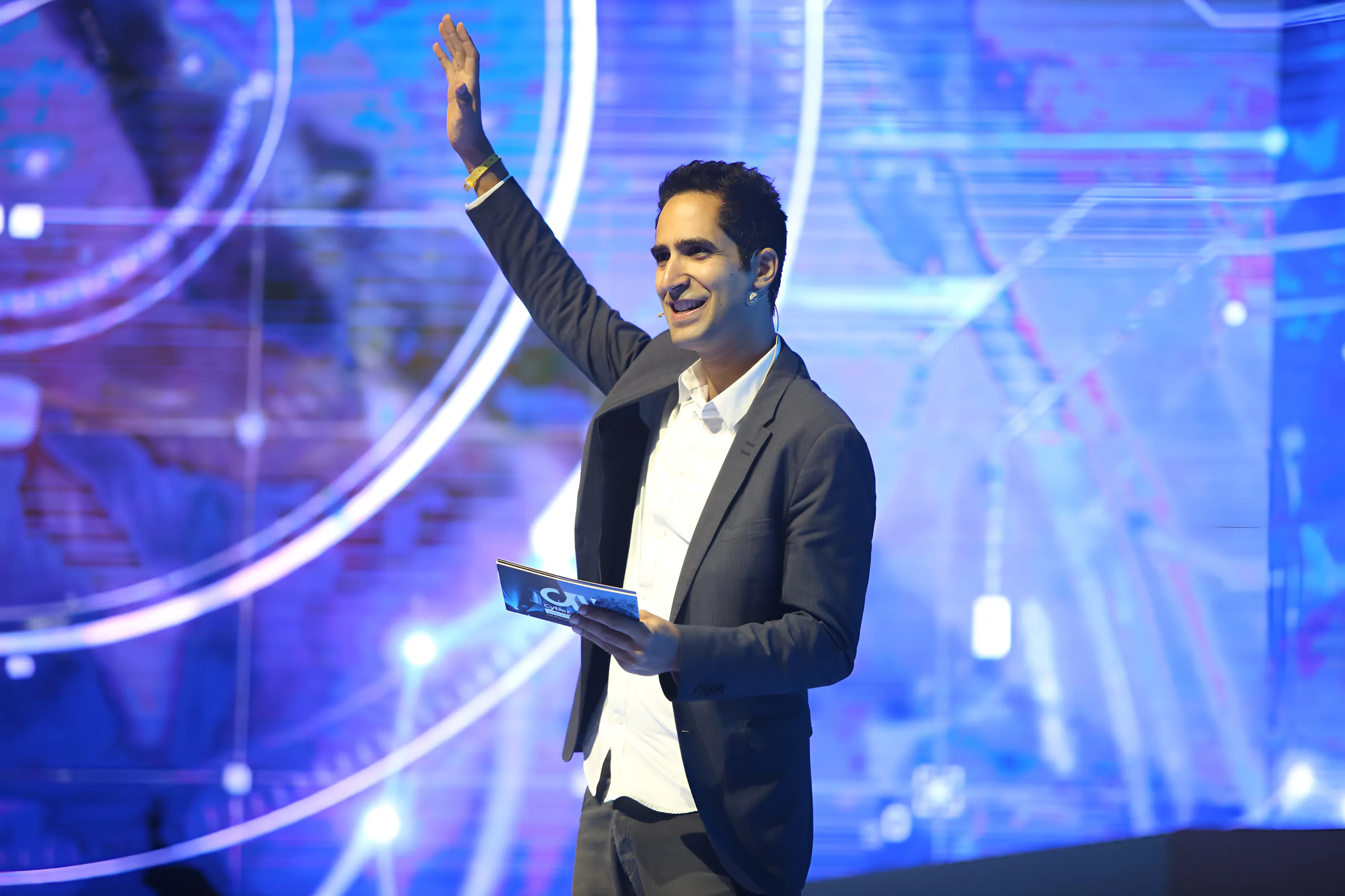 Menny Barzilay on the Cyber Week main stage, smiling and waving to the audience